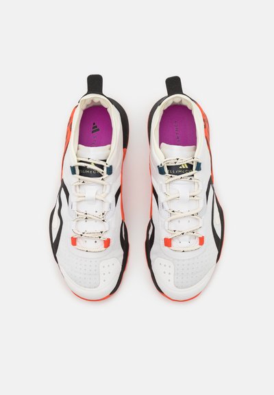 White athletic shoes with black and orange accents, featuring a textured upper, laces, and a purple insole branded with "STELLA McCARTNEY."