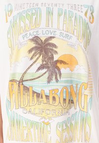 Hvit bomull T-skjorte med flerfarget grafisk design som inkluderer palmer, sol, havbølger, og tekstene: "Sunkissed in Paradise" og "Billabong."