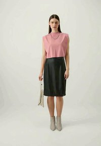 Top rosa sem mangas combinado com uma saia de couro preta e ajustada. A modelo segura uma clutch creme e usa botas cinza até o tornozelo. Design simples ao todo.