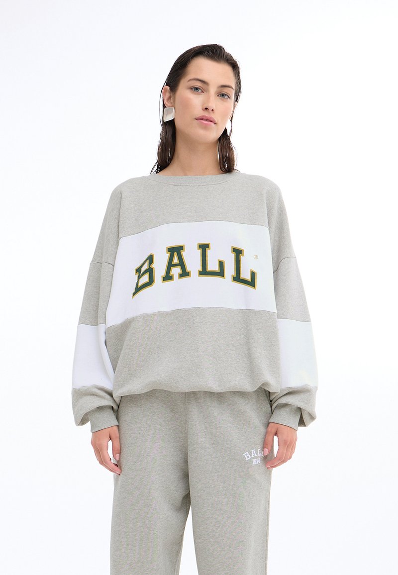 Felpa grigia con la scritta bianca e verde "BALL", design oversize, polsini a costine. Abbinata a pantaloni della tuta grigi coordinati con dettaglio del logo.