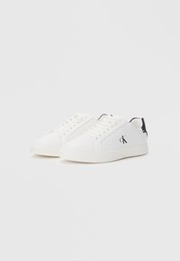 White sneakers with a smooth synthetic upper, contrasting black heel accents, round toe, and flat rubber sole; features logo detail on the side.