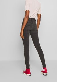 Dunne zwarte jeans met een hoge taille, voorzien van achterzakken met een gestikt ontwerp, gecombineerd met rode high-top sneakers.