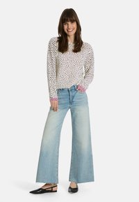 Helles Sweatshirt mit einem gepunkteten Muster und rosa Akzenten an den Ärmeln, kombiniert mit weitem, hellblauem Denim und schwarzen spitzen Ballerinas.