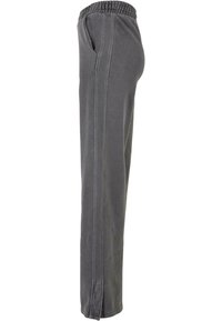 Pantalon de jogging gris avec une ceinture élastique, des poches latérales et des coutures surpiquées. Le tissu a une finition douce et texturée.