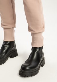 Svarta läderankelboots med tjocka, robusta sulor och elastiska sidopaneler, kombinerade med figurnära ljusrosa joggers med ribbade manschetter.