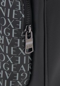 Borsa nera con materiale testurizzato e testo stampato grigio chiaro. Zip argentata con logo e dettaglio del tirante. Finitura liscia sul pannello laterale.