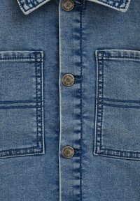 Mėlyna džinsinė marškiniai su dviem krūtinės kišenėmis, metaliniais mygtukais ir matomais siuvimo detalėmis. Audinys turi standartinę tekstūrą ir apdailą.