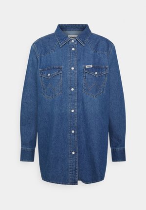 Niebieska dżinsowa koszula z długim rękawem, z przodu zapinana na guziki, z ostrym kołnierzem, dwie kieszenie na piersi z klapkami i guzikami oraz naszywką z logo Wrangler na prawej kieszeni.