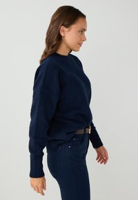 Maglione lavorato a maglia di colore blu navy con scollatura rotonda, polsini a coste e vestibilità rilassata, abbinato a pantaloni scuri slim-fit. Texture liscia.