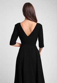 Czarna sukienka z dekoltem w kształcie litery V, rękawami o długości trzech ćwiartek i zwiewnym dołem. Gładka tekstura materiału oraz dyskretne zapięcie na suwak z tyłu.