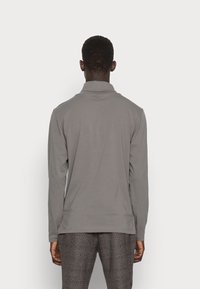 Langärmeliges Poloshirt in Grau aus glattem Material, mit umgeklapptem Kragen und geradem Saum, getragen zu karierten Hosen.