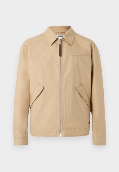 Μπεζ ανδρικό μπουφάν με φερμουάρ, μυτερό γιακά, δύο πλαϊνές τσέπες με καπάκι και μία μικρή τσέπη στο στήθος, σε απλό φόντο.