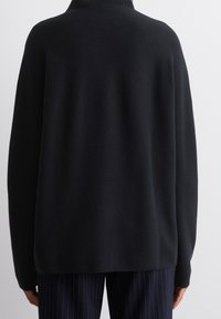 Pull noir de grande taille avec un col montant. Texture en maille, manches longues et coupe ample, associé à un pantalon à rayures fines.