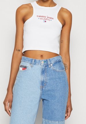 Personne portant un débardeur court blanc avec le logo "tommy jeans new york city" et un jean taille haute bicolore bleu.