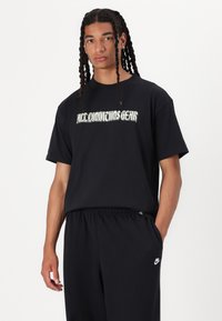 Čierne tričko s krátkym rukávom s nápisom "ALL CONDITIONS GEAR" vytlačeným bielou farbou. Bavlnený materiál. Kombinované s čiernymi nohavicami s logom Nike.