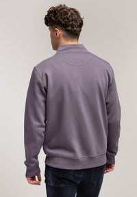 Fioletowy sweter wykonany z miękkiego materiału, z wysokim kołnierzem, długimi rękawami i ribbowym wykończeniem. Minimalistyczny design z czystymi liniami i bez widocznych wzorów.