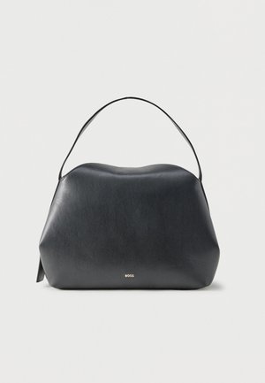 Sac à main en cuir noir avec une seule bandoulière et un petit logo doré "BOSS" à l'avant, sur un fond gris clair uni.