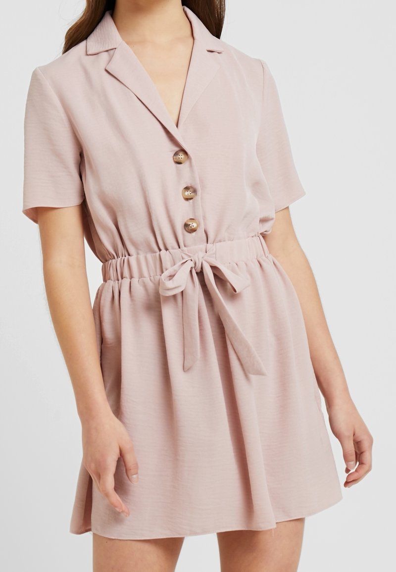 Abito rosa chiaro con maniche corte, colletto, cinque bottoni, vita elastica e cintura annodata in evidenza. Tessuto morbido con una vestibilità comoda.