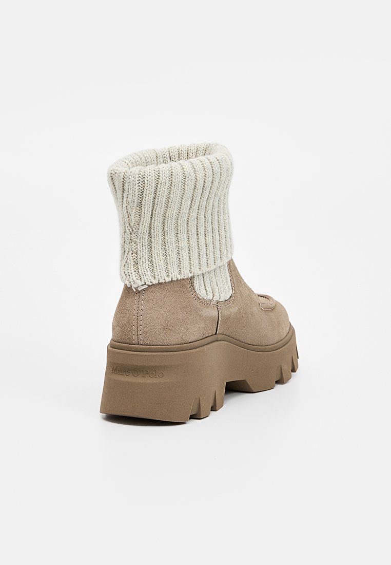 Braune Wildleder-Stiefeletten mit einer massiven, strukturierten Sohle und einem gerippten cremefarbenen Strickbund, ausgestattet mit seitlichen elastischen Einsätzen. Logo auf der Ferse eingestanzt.