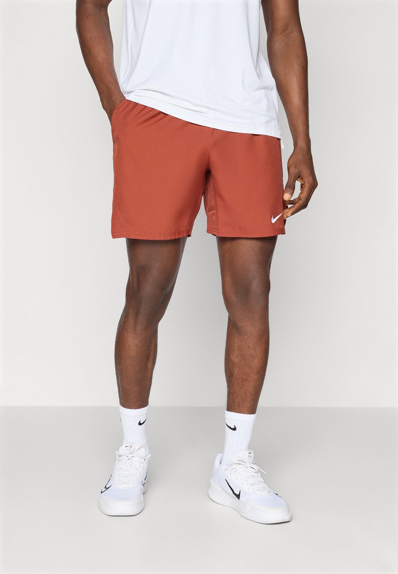 Rote Sportshorts mit glatter Textur, versehen mit einem schwarzen Nike-Logo. Kombiniert mit einem weißen T-Shirt und weißen Nike-Sneakern.