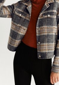 Rutet, cropped jakke i grå, brun og creme, lavet af tekstureret stof, med to brystlommer og sølvfarvede knapdetaljer.