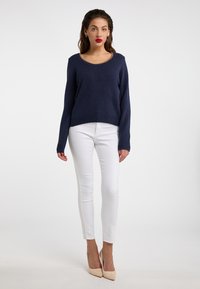 Tengerészkék pulóver kerek nyakkivágással és kötött szegéllyel, slim fit fehér farmernadrággal és nude magassarkúval párosítva. Sima textúra, modern dizájn.