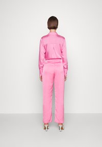 Conjunto de camisa e calças de satin rosa, com colarinho com botões, mangas longas e um corte descontraído, apresentando uma textura suave e detalhes mínimos.