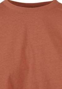 Gros plan d’un t-shirt uni en tissu coton couleur rouille avec un col rond et des coutures visibles autour du col.