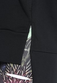 Tissu noir avec une petite fente laissant apparaître un matériau à motifs en dessous, avec des couleurs foncées et claires et un logo Nike Swoosh blanc.