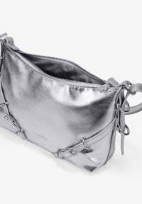 Bolso de mano metálico plateado con un acabado texturizado, cierre de cremallera y acentos decorativos de hardware en los laterales. Interior forrado visible.
