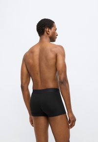 Boxer en coton noir avec une texture lisse et une ceinture élastique, vu de dos sur une personne aux cheveux courts.