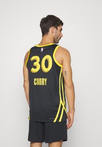 Camiseta de baloncesto negra con acentos amarillos y el número 30, con "CURRY" impreso debajo, hecha de un tejido transpirable y diseño sin mangas.