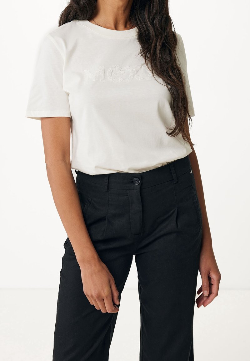 T-shirt couleur crème avec lettrage texturé "Mex", associé à un pantalon noir sur mesure. Manches courtes et col rond.