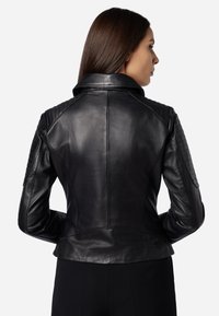 Schwarze Leder-Motorradjacke mit tailliertem Design, gesteppten Schulterakzenten und klassischem Reverskragen. Geschmeidige Textur und taillierte Form.