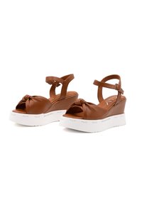 Sandali wedge in pelle marrone con design anteriore annodato, open-toe, cinturino alla caviglia e piattaforma bianca con marchio sul lato.