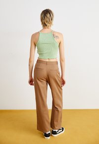 Grønn ribbet crop topp med bølgende kant, kombinert med brune vidde bukser. Svart-hvite sneakers fullfører antrekket.