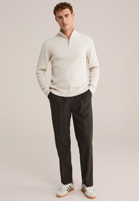 Pulover crem cu dungi, cu guler cu fermoar, combinat cu pantaloni eleganți închis și adidași deschiși. Design minimalist, textură moale.