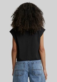 Fekete rövidített póló kapucnis ujjal, puha anyagból készült. Magas derekú kék farmer rövidnadrággal párosítva, hátoldalon zsebekkel.