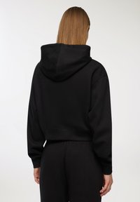 Czarna, krótka bluza z kapturem z troczkami, o miękkiej fakturze i długich rękawach. Projekt charakteryzuje się minimalistycznym stylem bez widocznych logo.