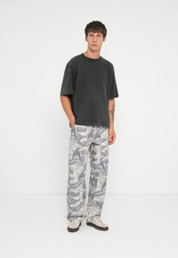 Black cotton oversized T-shirt paired with light gray, patterned wide-leg trousers and beige sneakers with brown soles.