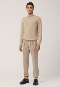 Maglione beige a collo alto e pantaloni beige chiaro. Il maglione ha una texture liscia; i pantaloni sono dalla vestibilità ampia. Stivali neri completano l'outfit.
