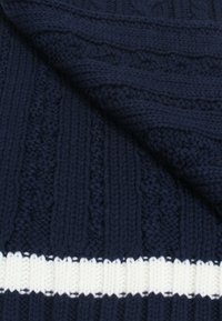 Tessuto di maglia blu navy con texture a coste e motivi intricati, caratterizzato da una striscia orizzontale bianca vicino al fondo.