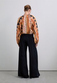 Multikleurige blouse met patroon en een geraffineerde achterzijde; gecombineerd met hoge zwarte wijde broek met zijsplitten en een gestructureerde afwerking.