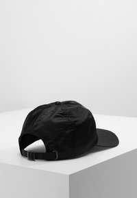 Sort baseball cap med en glat, skinnende overflade, justerbar rem bagpå og en buet skygge. Simpelt, minimalistisk design.