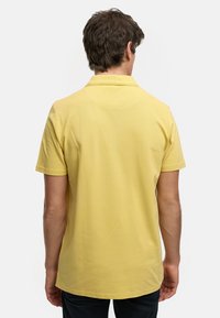 Kortärmad polo skjorta i ljus gul färg, med en klassisk krage och slät textur, rak fåll och utan synliga mönster eller detaljer.