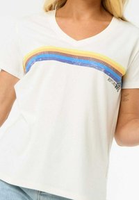 Weißes T-Shirt mit kurzen Ärmeln und V-Ausschnitt. Verfügt über horizontale Streifen in Gelb, Braun, Blau und Glitzer. Kleines Logo in der unteren linken Ecke.