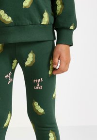 Grøn bomulds lounge sæt med trykte grønne ærtebølger og teksten "PEAS & LOVE." Inkluderer en sweatshirt og tætsiddende leggings.