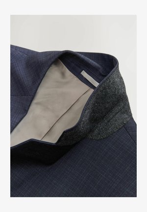 Blazer bleu marine avec un motif à carreaux, col en feutre et doublure beige à l'intérieur. Tissu texturé avec un design structuré.