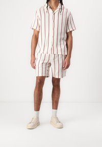 Conjunto de camisa de manga corta y pantalones cortos para hombre en crema con rayas verticales en color burdeos. Parte delantera abotonada, corte relajado, tejido texturizado. Calzado casual incluido.