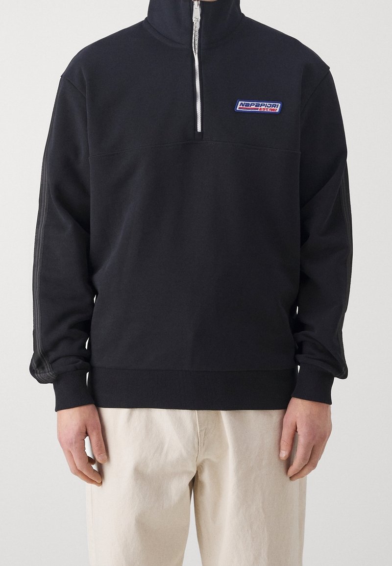 Sudadera negra con cremallera y cuello alto, que cuenta con puños y dobladillo acanalados, y un logotipo azul y blanco en el lado izquierdo del pecho. Tejido suave.